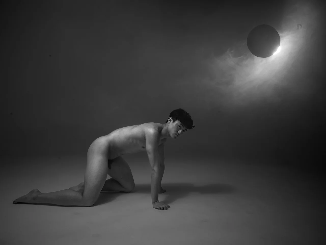 Schwarz-Weiß Portrait einer knienden Person unter dramatischem Licht mit Kunstball oben, minimalistische Komposition